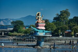 Statue of a goddess by the river in Haridwar, India, a scenic summer day with people around.